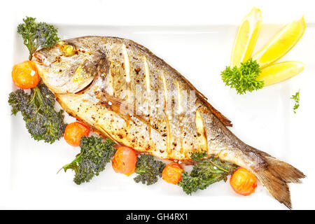 Roasted gilt head bream fish on a white plate with grilled tomatoes, kale and coarse grained salt. Stock Photo