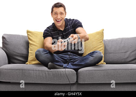 Cheerful young man seated on a sofa playing video games isolated on white background Stock Photo