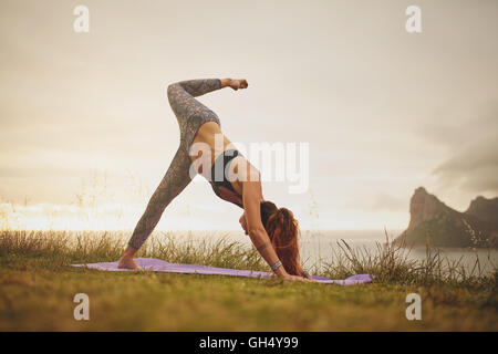 Side view shot of young woman practicing yoga outdoors on cliff. fitness female exercising in meadow. Stock Photo