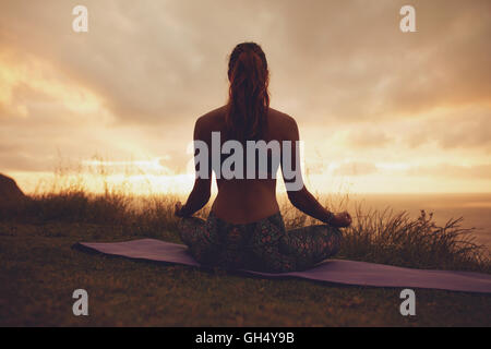 Silhouette rear view of young woman doing yoga meditation outdoors. fitness female model sitting on exercise mat in lotus yoga p Stock Photo