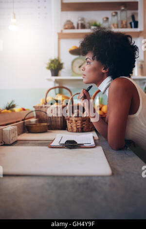 Side portrait of young woman standing at juice bar counter looking away and thinking. Thoughtful african female juice bar owner. Stock Photo