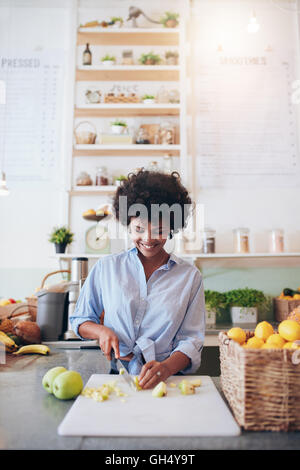 Vertical shot of african young woman cutting fruit on cutting board to make a fresh smoothie. African female bartender working a Stock Photo