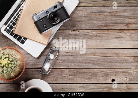 Desk table with laptop, camera, coffee and cactus on wooden table. Workplace. Top view with copy space. Stock Photo