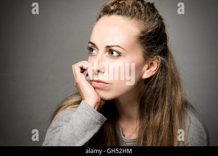 Young woman close up looking sorrowful, sad, thoughtful hand on chin looking in to the distance Stock Photo