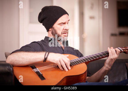 Man with beard playing guitar at home Stock Photo
