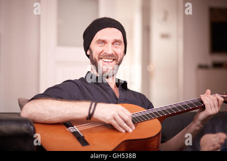 Hipster man with beard and hat playing guitar and smiling to camera Stock Photo