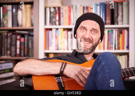 Hipster man with beard and hat playing guitar and smiling to camera Stock Photo