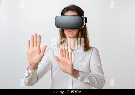 Single serious young woman in dark hair wearing large 3D virtual reality viewing device over face and reaching to feel something Stock Photo
