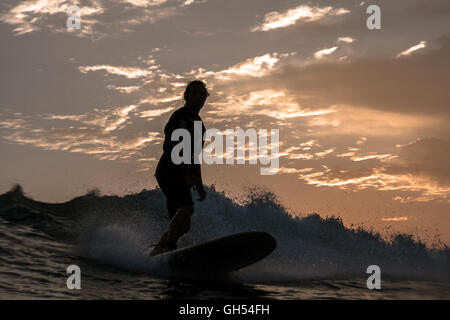 Silhouette of a surfer on his surfboard riding a wave at sunset Stock Photo