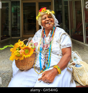 Cuban woman smoking cigar with flower basket and hat posing in Havana, Cuba Stock Photo