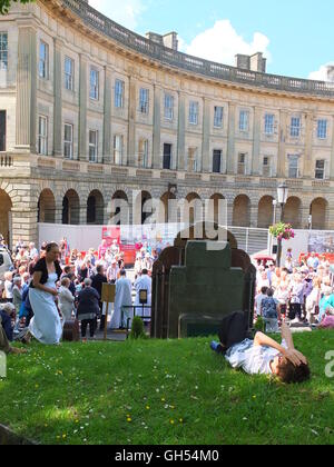 A boy lays on the grass as the well dressing at St Ann's Well, Buxton, is blessed. Backdrop of the town's Georgian Crescent. Stock Photo