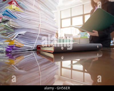 Pile of unfinished documents on office desk with businesswoman background Stock Photo