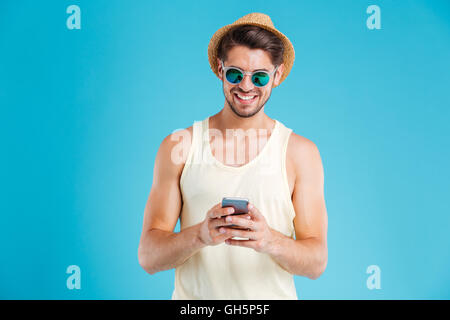 Happy young man in hat and sunglasses using smartphone Stock Photo