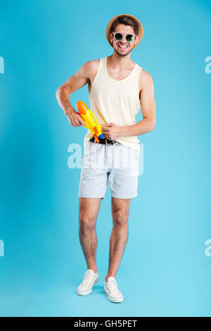 Cheerful handsome young man standing and posing with water gun Stock Photo
