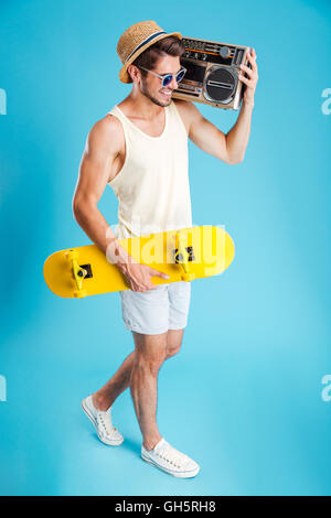 Happy young man with boombox walking and holding skateboard Stock Photo