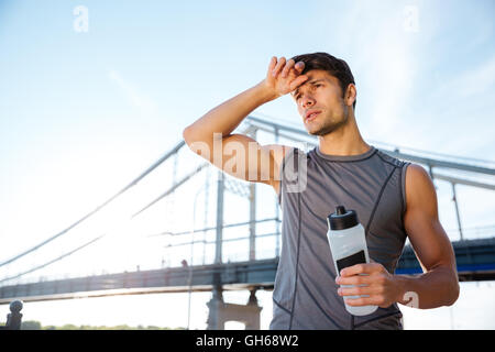 Handsome young sports man resting after running and holding water bottle at the bridge Stock Photo