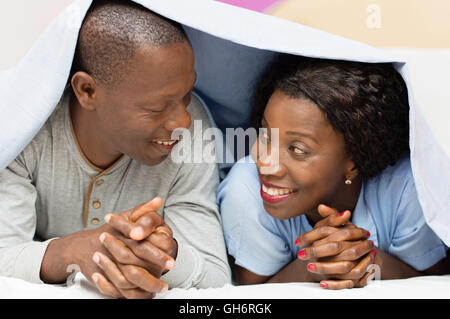 young couple lying under the cover looks, smiling. Stock Photo