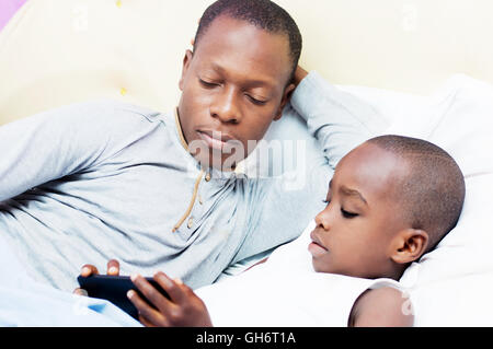 Dad looks at his child using mobile phone in bed Stock Photo