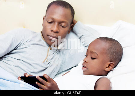 Dad looks at his child using mobile phone in bed Stock Photo