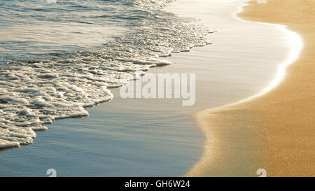 Soft sea waves rushing on sandy beach at sunset Stock Photo