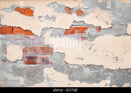 Old brick wall with damaged stucco and yellow paint layers, background photo texture Stock Photo