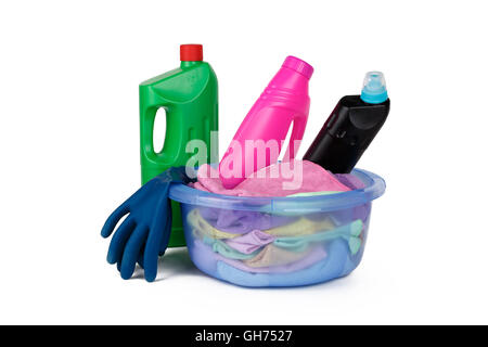 Plastic colorful detergent bottles, blue rubber glove and cleaning brush in laundry basket with clothes and towels, isolated on  Stock Photo