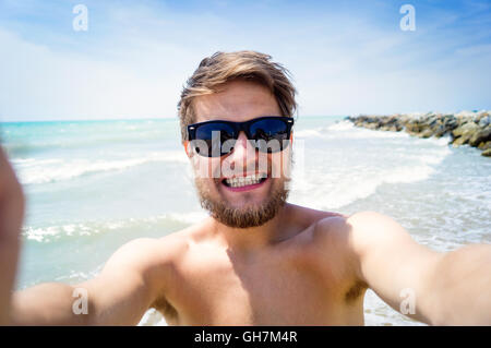 Hipster man on beach, smiling, taking selfie, sunny summer Stock Photo