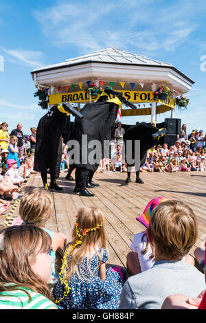 Popular Hobby Horse Club event for families and children at the Broadstairs folk week. Ossies, black bird type creatures each with a man inside, dancing on the deck by the bandstand, surrounding by audience of children and parents. Stock Photo