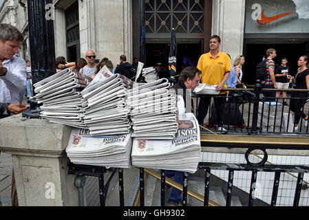 Free newspapers.  Copies of The Evening Standard piled up on railing at Oxford Circus Station, vendor in background, Central Lon Stock Photo