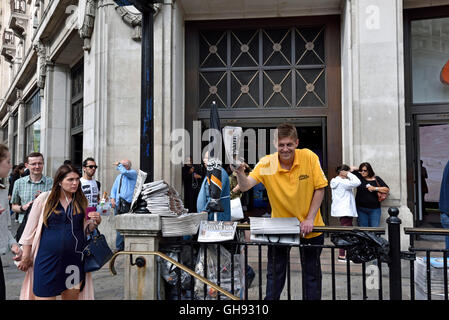 Free newspapers.  Copies of The Evening Standard piled up on railing at Oxford Circus Station, vendor in background, Central Lon Stock Photo