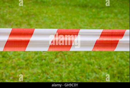 Red and white warning tape on green grass background Stock Photo