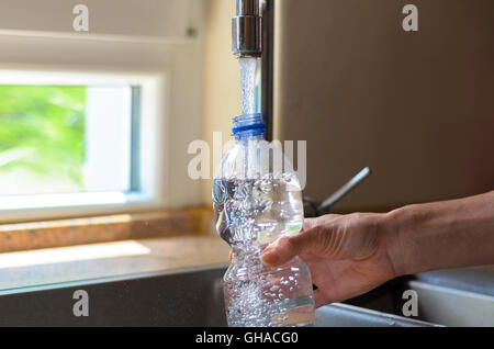 Woman filling a plastic bottle with water from the faucet in the kitchen with a close up view on the running water, air bubbles Stock Photo