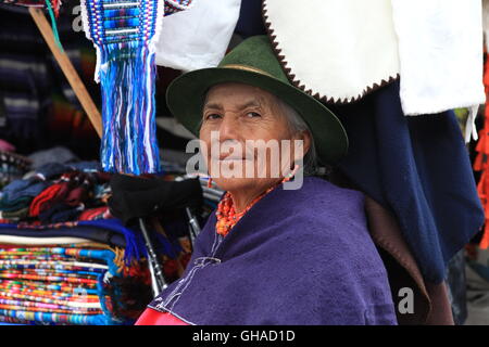 An elderly Ecuadorian woman in traditional dress, sits by her handmade clothes stall in Otavalo Market Stock Photo