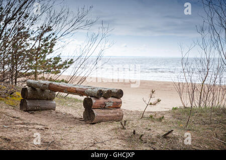Empty rough wooden bench stands on Baltic Sea coast in spring season. Coastal landscape Stock Photo