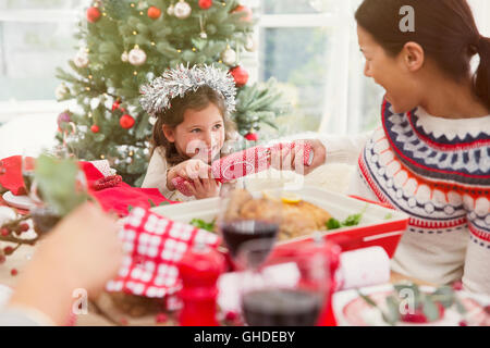 Mother and daughter pulling Christmas cracker at dinner table Stock Photo