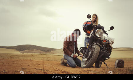 Young couple repairing motorcycle in remote countryside field Stock Photo