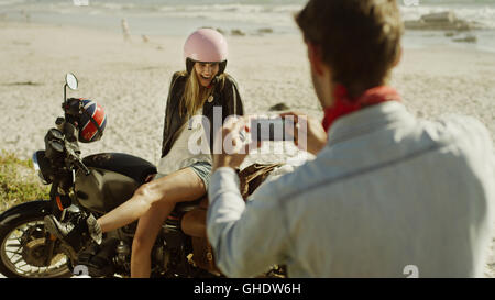 Young man photographing woman on motorcycle at beach Stock Photo