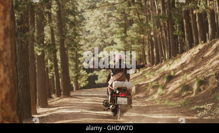 Exuberant young woman riding motorcycle on dirt road in woods Stock Photo