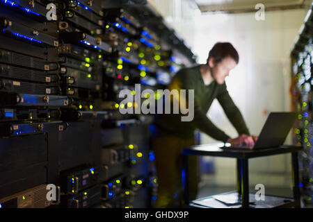Server room technician working at laptop in corridor Stock Photo