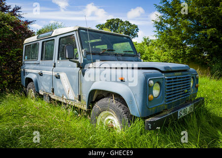 Old Land Rover Defender retired in the long grass awaiting restoration Stock Photo