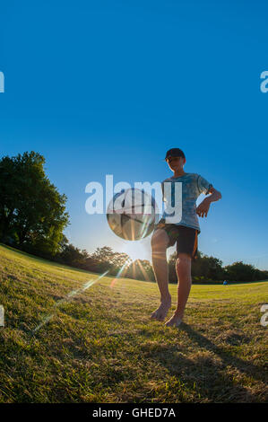 A boy playing football, performing freestyle tricks in an urban park at play Stock Photo