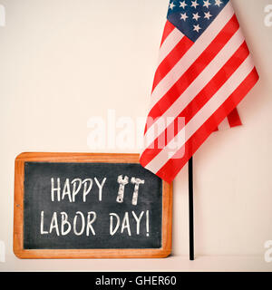 a wooden-framed chalkboard with the text happy labor day written in it and a flag of the United States, against an off-white bac Stock Photo