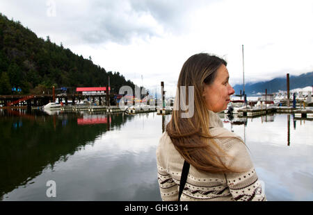 Middle aged Woman Waiting for the Ferry at Horseshoe Bay, BC Dock with View of a Local Fishing Boat Marina and Inlet Stock Photo