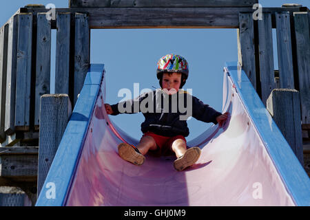 A scared boy (4 yrs old) sat looking down a long slide