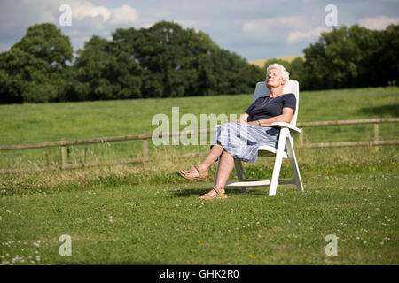 Senior woman outside relaxing in chair in field UK Stock Photo