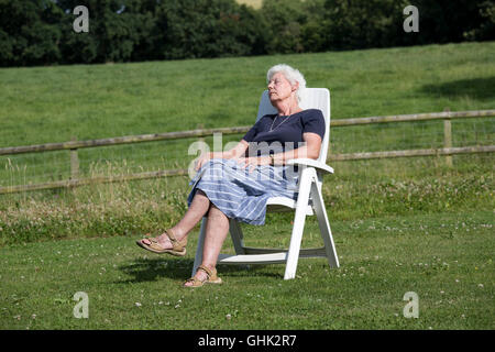 Senior woman asleep outside relaxing in chair in field UK Stock Photo