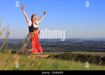 A German Woman in Bavarian Dirndl jumping on the meadow Stock Photo