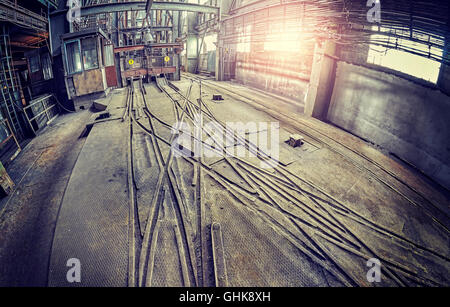 Vintage toned fisheye lens picture of abandoned industrial hall interior with trolley tracks. Stock Photo