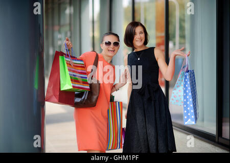 Beautiful young women show bright multi-coloured packages with purchases. They look into a camera and cheerfully smile. Girlfrie Stock Photo