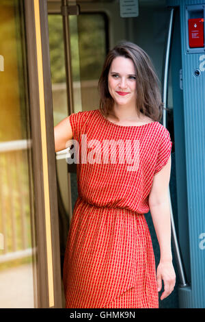 young woman in red dress standing in door of train wagon Stock Photo